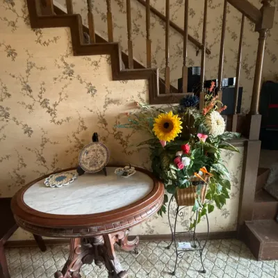 Sale Photo Thumbnail #45: Antique round marble-top accent table with carved wooden pedestal base, paired with a floral arrangement on a wire plant stand.