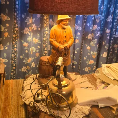 Sale Photo Thumbnail #62: Vintage nautical fisherman table lamp featuring a figurine in a raincoat alongside a brass tea kettle and miniature penny-farthing bicycle decorative accent.
