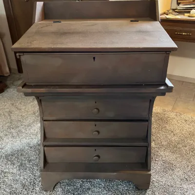 Sale Photo Thumbnail #47: Vintage dark-stained wooden slant-top clerk's desk featuring a lift-top writing surface and three lower storage drawers with wooden knobs.