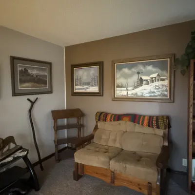 Sale Photo Thumbnail #57: Rustic wooden loveseat with tan upholstery and a colorful crocheted throw, displayed alongside framed landscape art prints and small wooden furniture pieces.