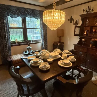 Sale Photo Thumbnail #38: Traditional dark wood dining room set with matching captain's chairs, fully set with fine china, illuminated by a tiered glass chandelier.