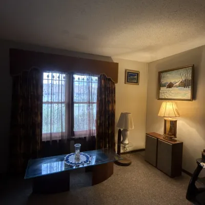 Sale Photo Thumbnail #55: Living room setup featuring a mid-century glass-top coffee table with curved wooden base, vintage floor and table lamps, paired stereo speakers, and framed wall artwork.