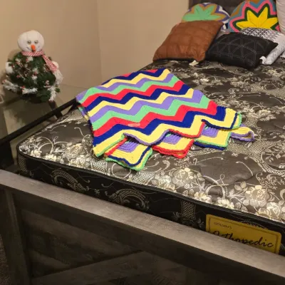 Sale Photo Thumbnail #15: Handmade chevron crochet afghan blanket in vibrant primary colors resting on a modern rustic wood bed frame.