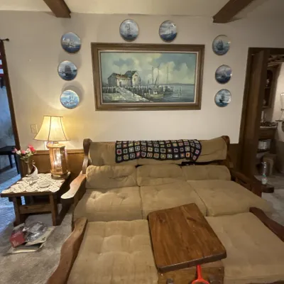 Sale Photo Thumbnail #52: Rustic rustic wood frame sectional sofa with tan tufted upholstery, paired with a matching coffee table and a large framed nautical landscape painting with decorative wall plates.