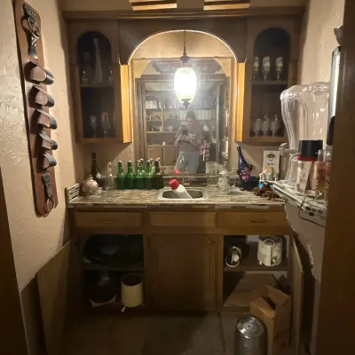 Sale Photo Thumbnail #46: Built-in wooden home wet bar with arched mirror, upper glassware shelving, small sink, and overhead ceiling-mounted glass racks.