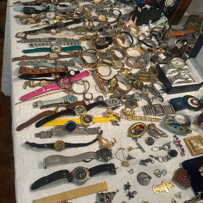 Sale Photo Thumbnail #119: Large collection of vintage to modern wristwatches, watch bands, costume jewelry brooches, and pendants laid out on a white tablecloth.