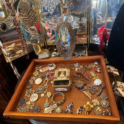 Sale Photo Thumbnail #76: Wooden display tray filled with vintage brooches, pins, and costume jewelry, set alongside hanging necklaces and purse accessories.