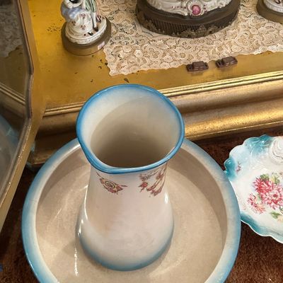 Sale Photo Thumbnail #33: Vintage ceramic wash basin and pitcher set with blue trim and floral transfers, shown alongside various porcelain figurines in a display cabinet.