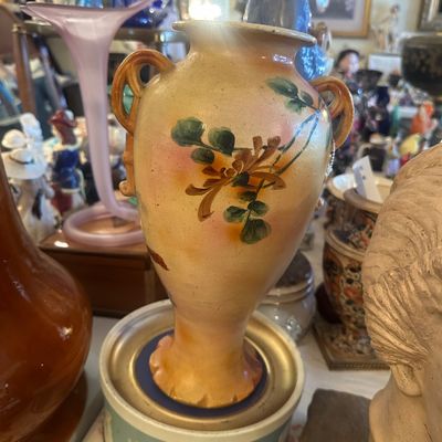 Sale Photo Thumbnail #100: Hand-painted double-handled ceramic vase featuring floral motifs in matte earth tones, displayed alongside various decorative collectibles.