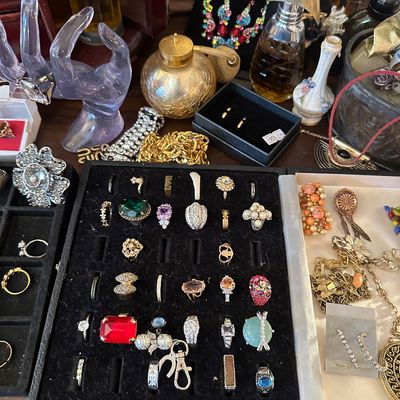 Sale Photo Thumbnail #13: Collection of vintage costume jewelry displayed in trays alongside perfume atomizers, glass hand ring holders, and loose necklaces.