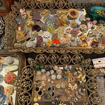 Sale Photo Thumbnail #17: Large collection of vintage costume jewelry, including brooches and clip-on earrings, displayed on ornate filigree gold-tone mirrored trays.