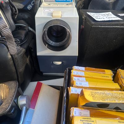 Sale Photo Thumbnail #88: Vintage Canon Slidester 300 8mm film projector accompanied by various boxed film rolls and camera accessories.