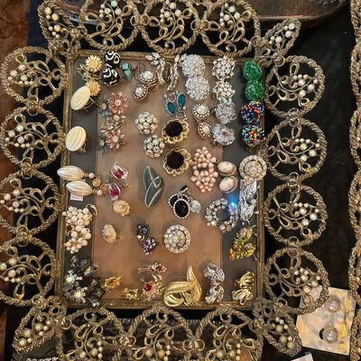 Sale Photo Thumbnail #79: Collection of vintage costume jewelry, including clip-on and pierced earrings, brooches, and rhinestone bracelets arranged on an ornate filigree tray.