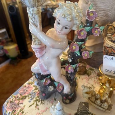 Sale Photo Thumbnail #99: Vintage ceramic cherub candlestick holder featuring a painted cherub figure holding a pillar beside a flowering tree branch.