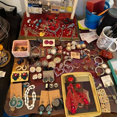 Sale Photo Thumbnail #19: Large collection of assorted costume jewelry including dangle earrings, beaded necklaces, brooches, and clip-on earrings displayed on a tabletop stand and trays.