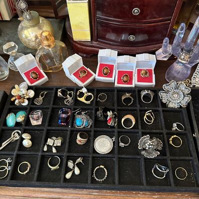 Sale Photo Thumbnail #12: Collection of assorted costume jewelry including rings, earrings, and brooch pins displayed in a compartmentalized tray alongside boxed tiger's eye rings and perfume bottles.
