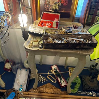 Sale Photo Thumbnail #5: Collection of vintage costume jewelry, cufflinks, and vanity items displayed on a small painted tray table, accompanied by a framed floral print and leather travel accessories.