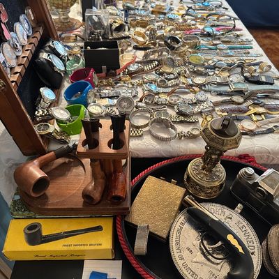 Sale Photo Thumbnail #4: Large collection of vintage estate jewelry, wristwatches, smoking pipes on a wooden stand, and miscellaneous trinkets displayed on a table.