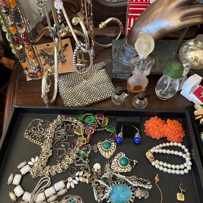 Sale Photo Thumbnail #11: Collection of vintage costume jewelry, featuring bold statement necklaces, earrings, and beaded pieces arranged on a display tray and stand alongside decorative perfume bottles.