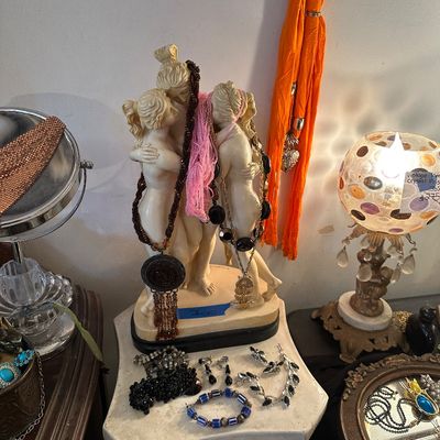 Sale Photo Thumbnail #14: Neoclassical style Three Graces statue draped in beaded necklaces, set on a pedestal surrounded by costume jewelry and a mosaic globe lamp.