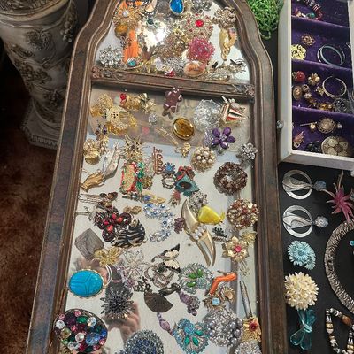 Sale Photo Thumbnail #77: Large collection of vintage costume jewelry brooches, pins, and accessories displayed on an ornate framed mirror and in a jewelry box.