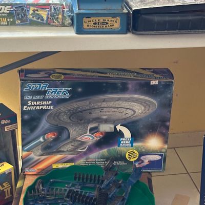 Sale Photo Thumbnail #44: Vintage Uncle Sam's 3-coin register bank displayed above a boxed 1990s Playmates Star Trek: The Next Generation Starship Enterprise toy.