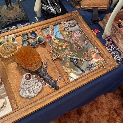 Sale Photo Thumbnail #7: Assorted vintage costume jewelry, brooches, and vanity accessories arranged in a gilded ornate frame on a display table.