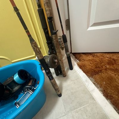 Sale Photo Thumbnail #68: Collection of vintage fishing rods and reels leaning against a wall alongside a blue plastic tub filled with additional reels and fishing accessories.