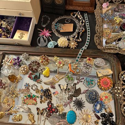 Sale Photo Thumbnail #16: Large collection of vintage costume jewelry, featuring colorful brooches, pins, and necklaces displayed on mirrors and in small jewelry chests.