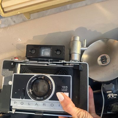 Sale Photo Thumbnail #85: Vintage Polaroid 195 Land Camera featuring a Tomioka Japan f/3.8 114mm lens, complete with attached flash bulb mechanism and reflector dish.