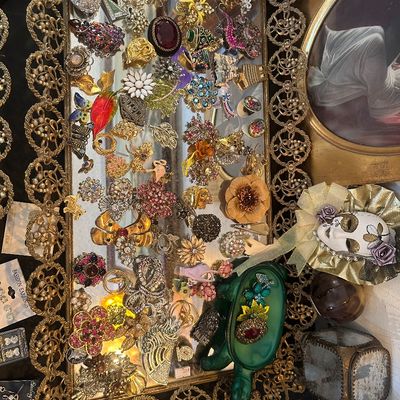 Sale Photo Thumbnail #78: Collection of vintage costume jewelry brooches, pins, and accessories displayed on an ornate mirrored tray.