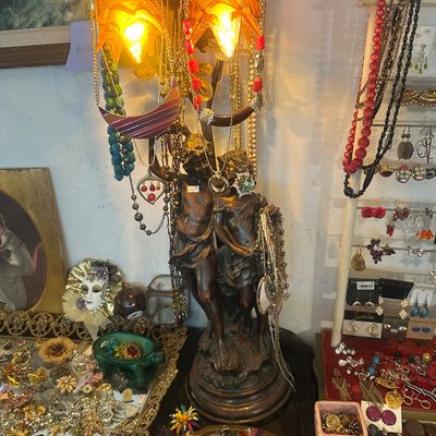 Sale Photo Thumbnail #82: Vintage bronze-finish figural table lamp depicting two cherubs with amber art glass shades, draped in assorted costume jewelry, displayed alongside additional brooches, necklaces, and earrings.