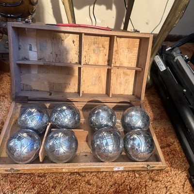 Sale Photo Thumbnail #90: Vintage French pétanque or bocce ball set featuring eight engraved chrome-plated steel boules in a custom wooden carrying case with a red handle.