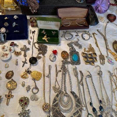 Sale Photo Thumbnail #20: Assortment of vintage costume jewelry, eyeglasses, and accessories arranged on a white tablecloth, including statement necklaces, rings, and religious pendants.