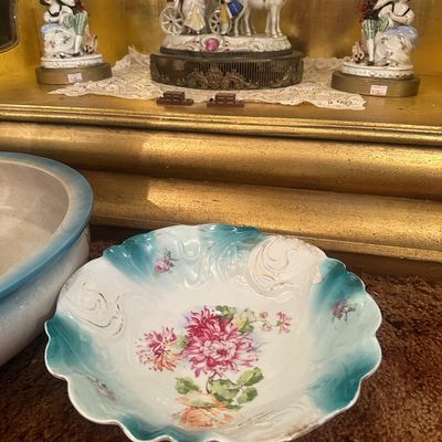 Sale Photo Thumbnail #97: Antique floral porcelain bowl with scalloped teal edges alongside vintage European-style porcelain figurines in a display cabinet.