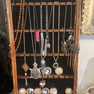 Sale Photo Thumbnail #109: Wooden display rack featuring assorted vintage fashion necklaces, including a large turtle pendant, amber-colored beads, and various chains alongside framed commemorative coins.