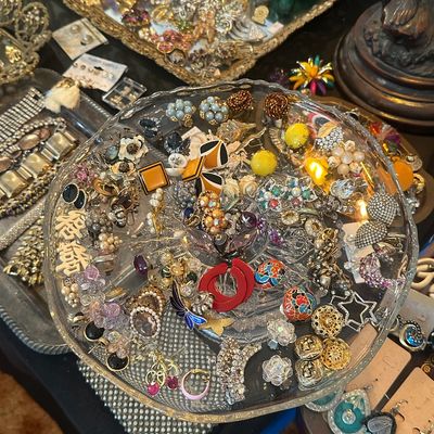 Sale Photo Thumbnail #107: Large assortment of vintage costume jewelry, including brooches, clip-on earrings, and beaded pieces, displayed on cut-glass trays.