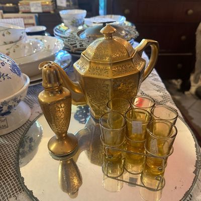 Sale Photo Thumbnail #118: Vintage gold-gilded ornate teapot with matching shaker and a caddy set of six amber glass shot glasses, presented on a circular mirror tray.