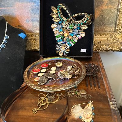 Sale Photo Thumbnail #9: Collection of vintage costume jewelry, including an ornate rhinestone collar necklace in a display box, buttons on an iridescent carnival glass plate, hair combs, and gold-tone chain necklaces.