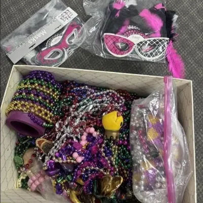Sale Photo Thumbnail #22: Box filled with colorful Mardi Gras bead necklaces and costume accessories, alongside packaged feather masquerade masks.