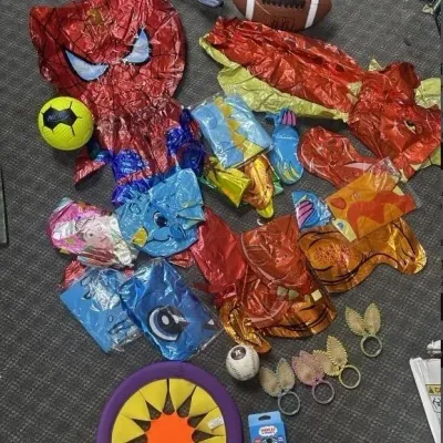 Sale Photo Thumbnail #151: Assortment of children's party supplies and toys, including deflated Mylar balloons, sports balls, costume accessories, and a frisbee.