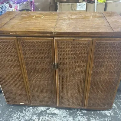 Sale Photo Thumbnail #160: Vintage mid-century wooden stereo console with woven cane door panels and a flip-top lid, showing some surface wear.