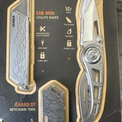 Sale Photo Thumbnail #141: Packaged Gerber knife set featuring a Ripstop I clip folding knife, EAB Mini utility knife, and Shard DT keychain tool, all unused in original blister packaging.