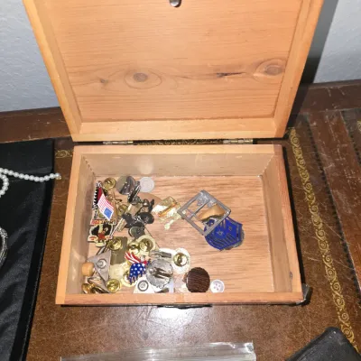 Sale Photo Thumbnail #28: Open wooden trinket box filled with an assortment of vintage lapel pins, military-style insignia, buttons, and small metal novelties.