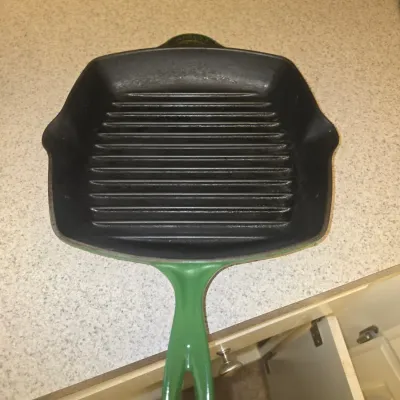 Sale Photo Thumbnail #115: Le Creuset green enameled cast iron square grill pan featuring dual pour spouts and a black matte interior surface.