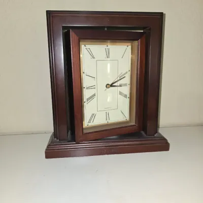 Sale Photo Thumbnail #44: Swivel mantle clock housed in a dark wood frame with a rectangular face and Roman numerals.