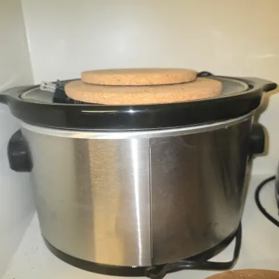 Sale Photo Thumbnail #119: Stainless steel oval slow cooker with black handles and a removable ceramic insert, stacked with two round cork trivets.