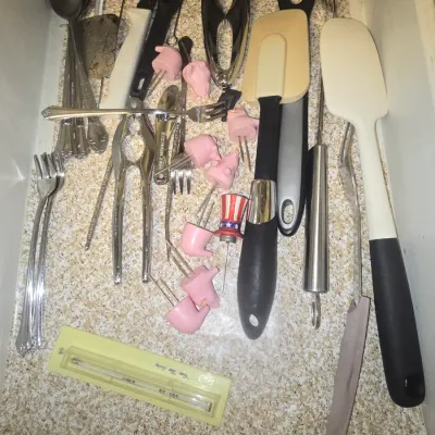 Sale Photo Thumbnail #116: Kitchen drawer full of miscellaneous utensils, including rubber spatulas, stainless steel spoons and forks, nutcrackers, novelty pig corn holders, and a vintage kitchen thermometer.