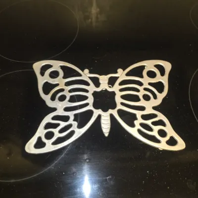 Sale Photo Thumbnail #114: Cast aluminum butterfly-shaped trivet resting on a glass stovetop.