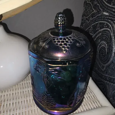 Sale Photo Thumbnail #14: Iridescent blue carnival glass jar with lid featuring embossed grape and leaf motifs, topped with a pinecone or fruit finial.